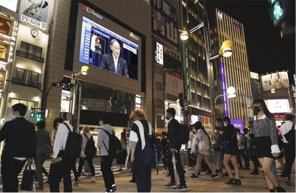 9일 저녁 퇴근길 인파로 붐비는 도쿄 신주쿠 거리의 한 건물 벽면 TV에 긴급사태 연장 관련 기자회견을 하는 스가 요시히데 총리의 모습이 비치고 있다.